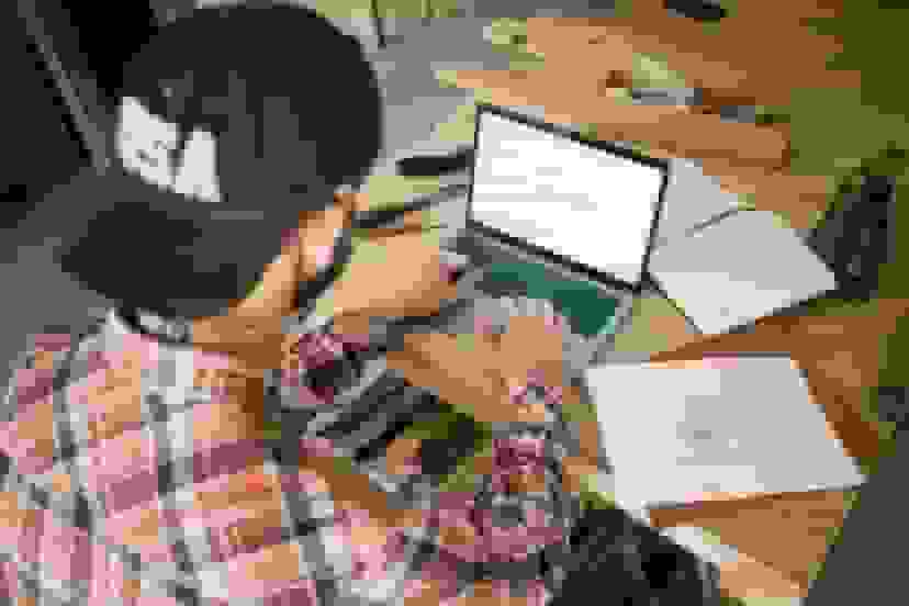 Small business owner wearing a baseball cap, working on a laptop to manage insurance records and business operations.