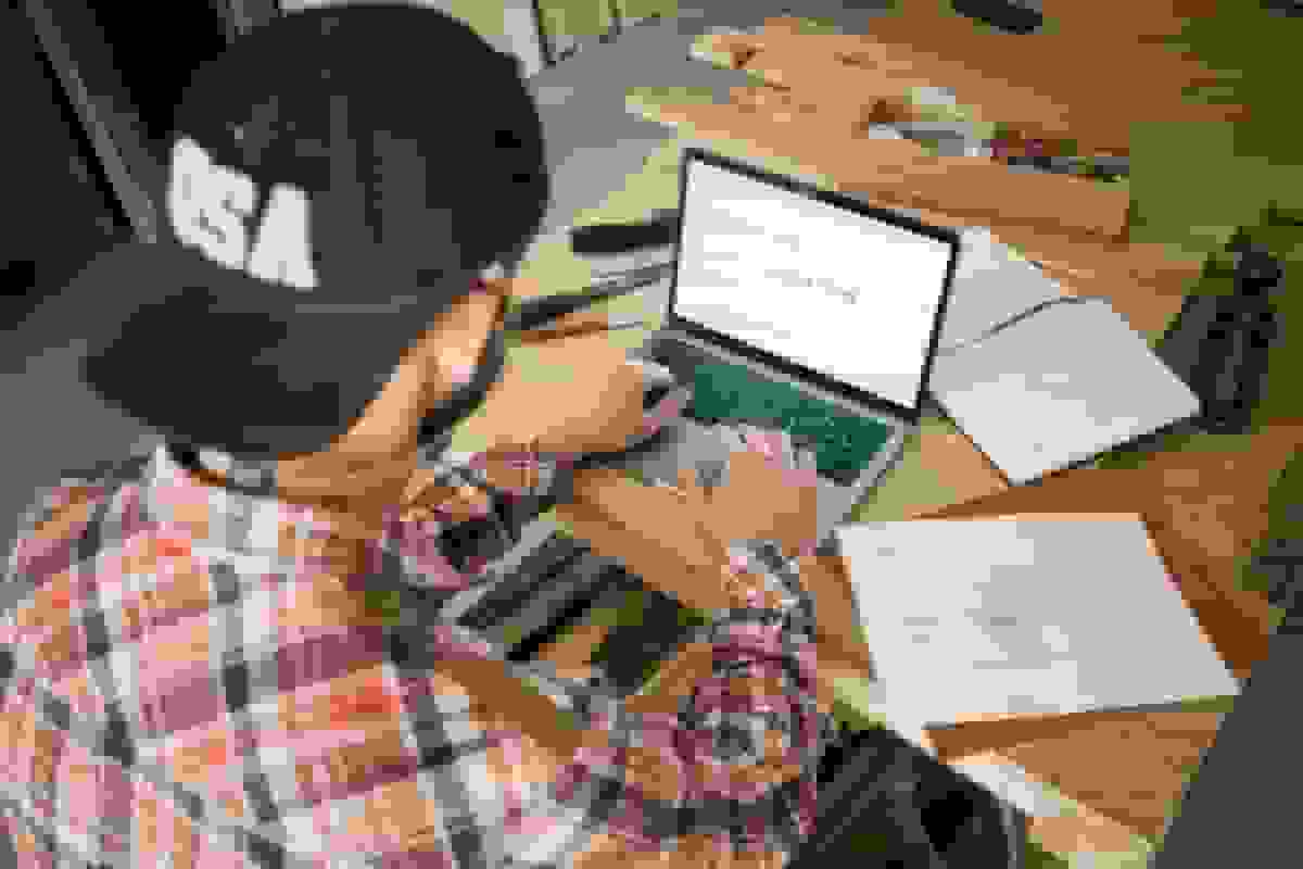 Small business owner wearing a baseball cap, working on a laptop to manage insurance records and business operations.